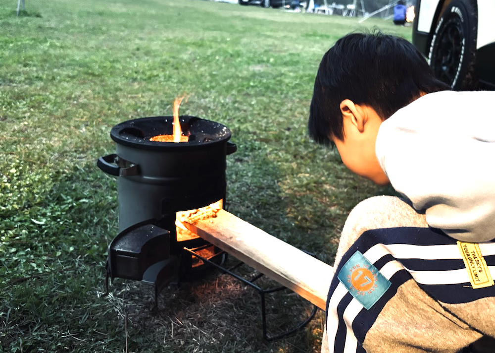 ロケットストーブの火守りをする子ども 